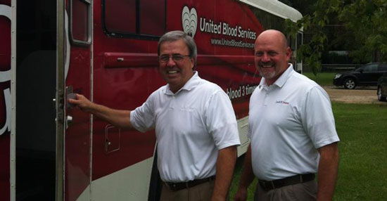 2 lard oil company employees in uniform smile while opening a United Blood Services bus door